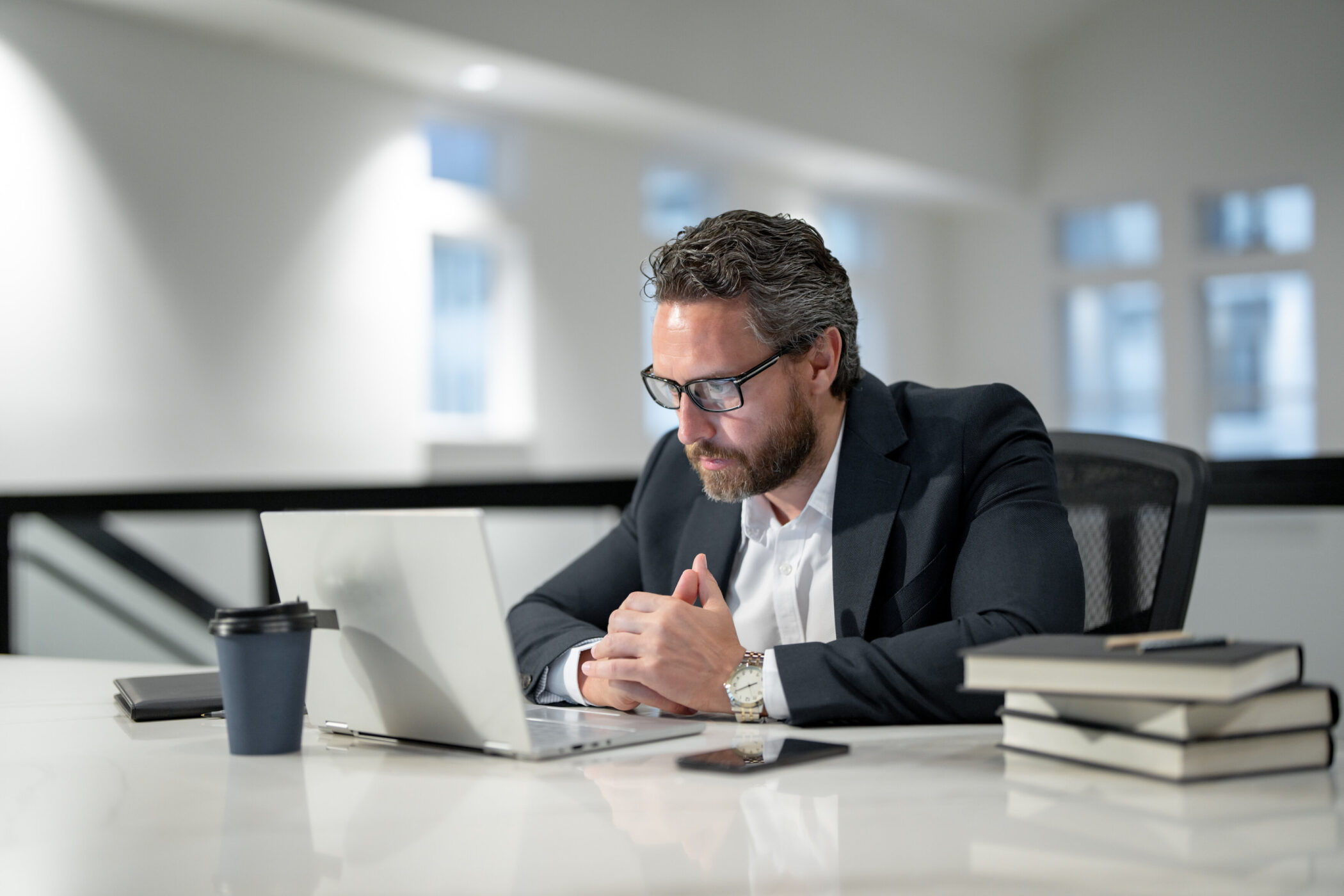 Mann am Schreibtisch mit Laptop, Notizbuchstapel und Kaffeebecher.