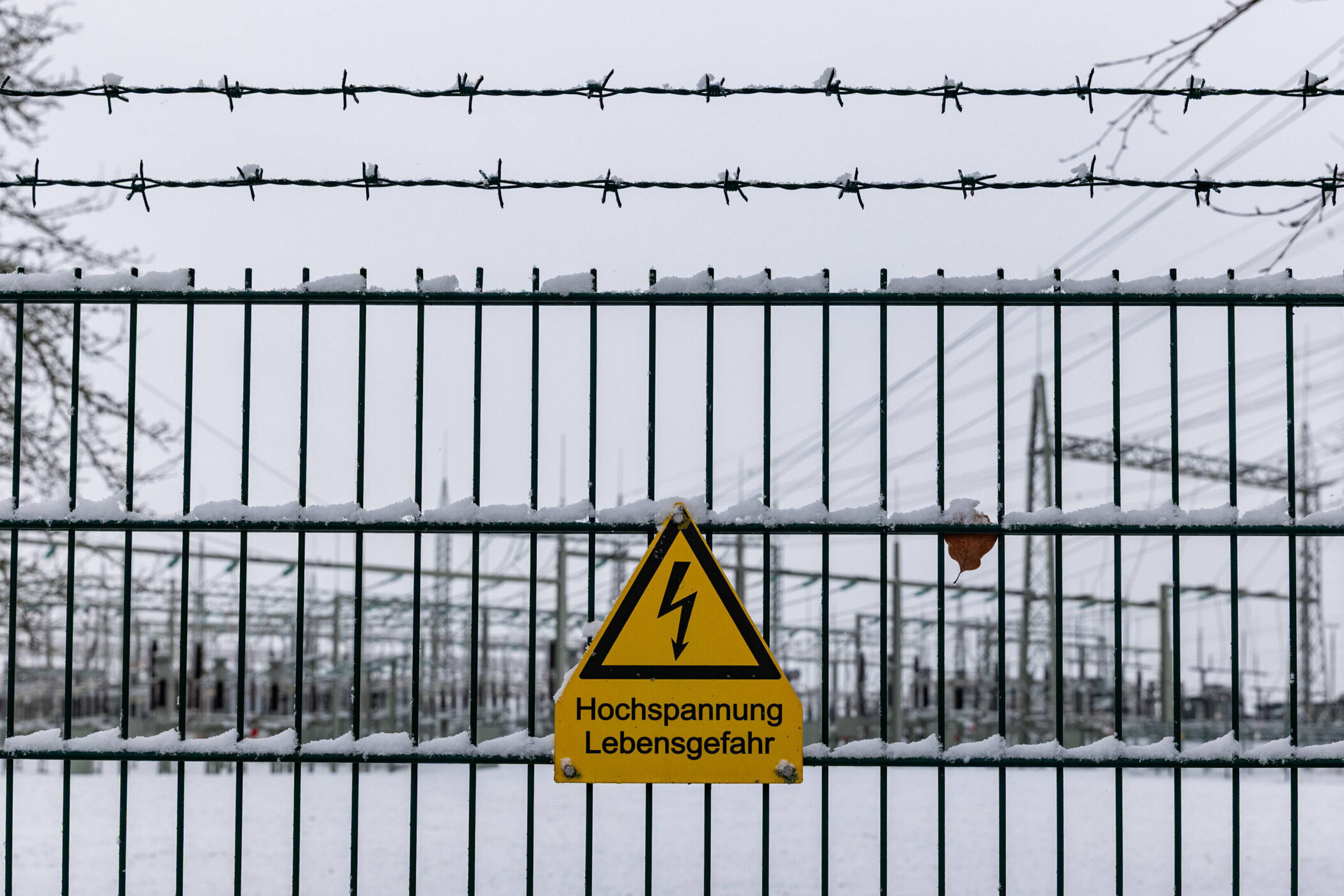 Zaun mit Stacheldraht, Schneebedeckung, Warnschild: "Hochspannung Lebensgefahr".