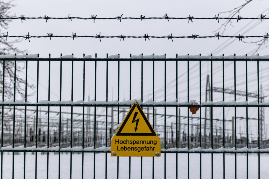 Zaun mit Stacheldraht, Schneebedeckung, Warnschild: "Hochspannung Lebensgefahr".