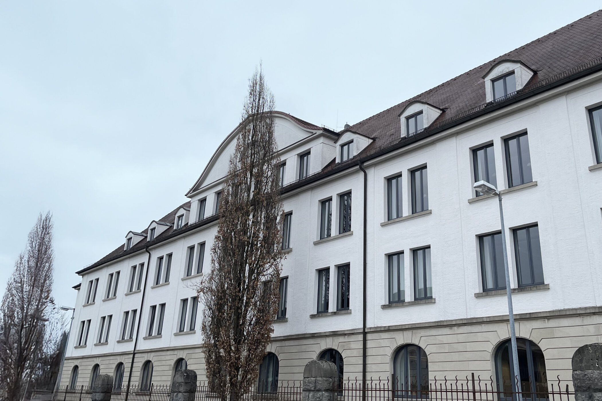 Weißes Gebäude mit mehreren Fenstern und einem Baum davor.