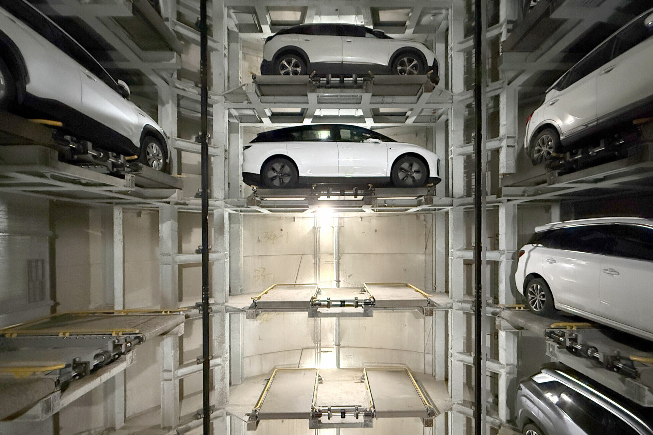 Mehrstöckiges automatisiertes Parksystem mit mehreren weißen Autos auf Plattformen.