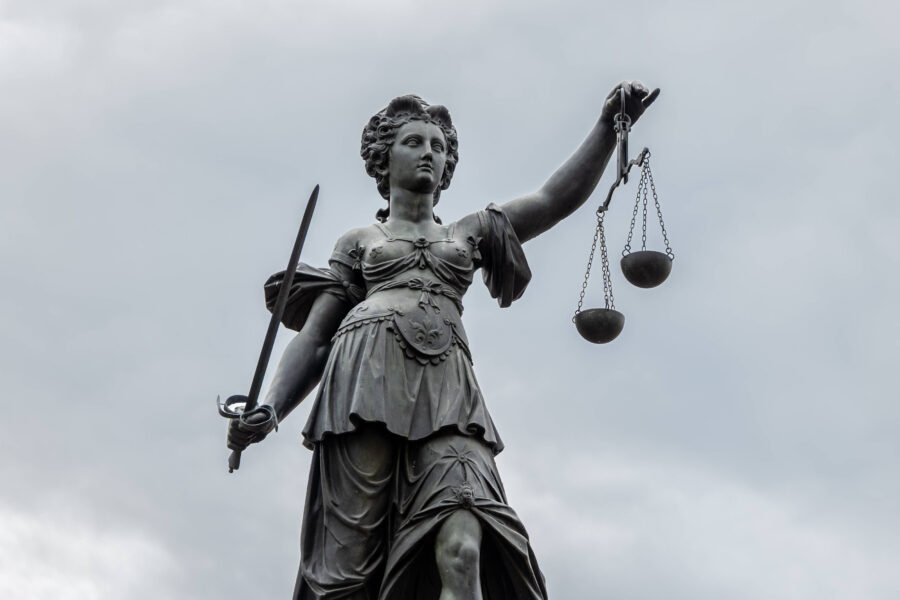 Statue einer Frau mit Schwert und Waage vor bewölktem Himmel.