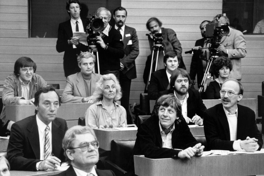 Mehrere Personen in einem Konferenzraum, einige mit Kameras.