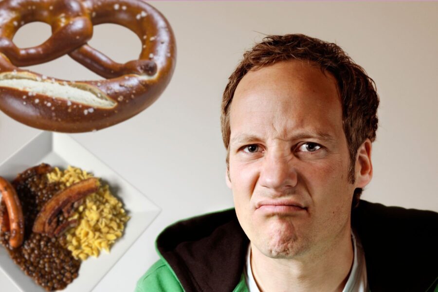 Mann mit missbilligendem Gesichtsausdruck, Brezel und Teller mit Essen.