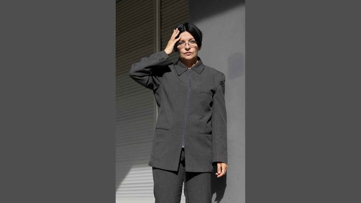 Eine Person in grauem Anzug berührt mit der Hand ihren Kopf.