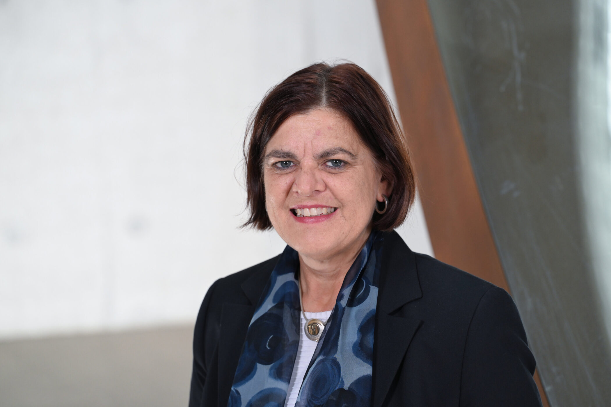 Eine Frau mit dunklem Haar und Blazer lächelt in die Kamera.