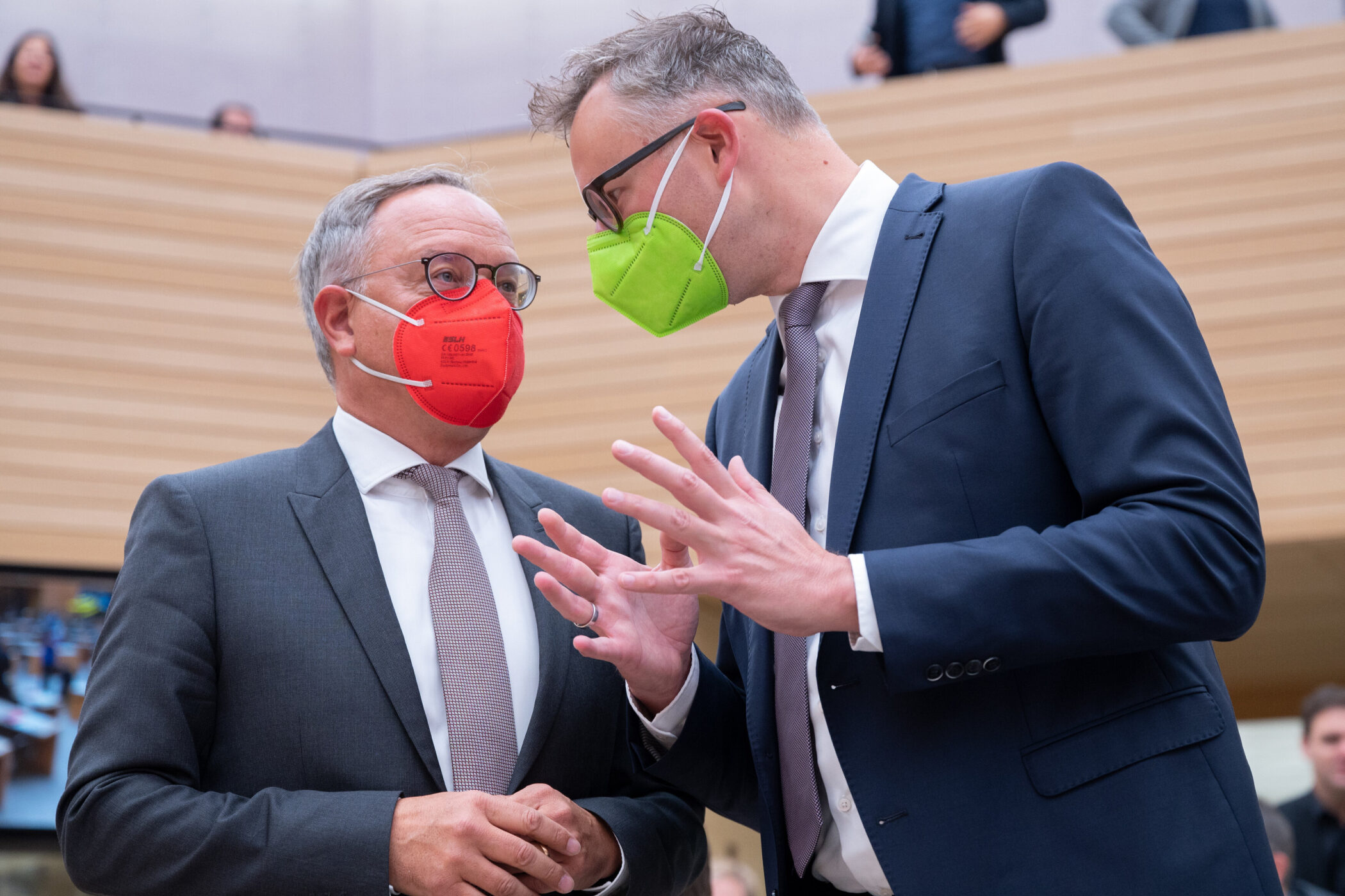 Zwei Männer im Anzug mit farbigen Masken im Gespräch.