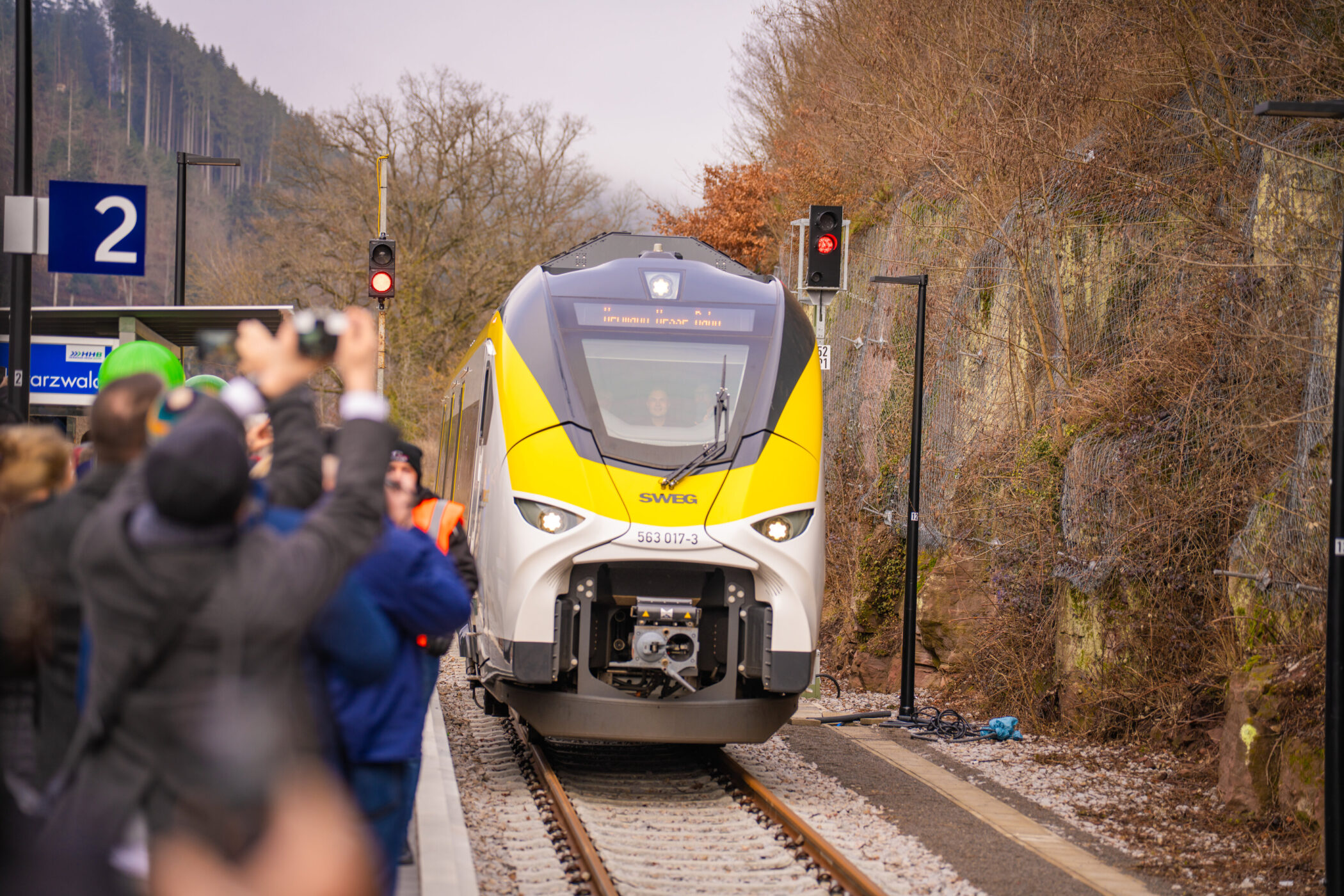 Zug fährt in Bahnhof ein, Menschen fotografieren, Signal zeigt Rot.