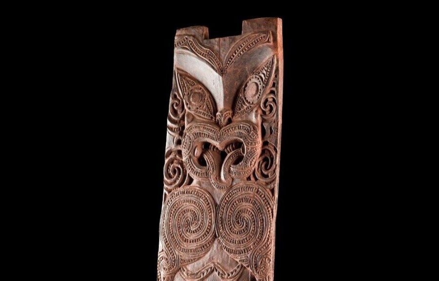 Holzskulptur mit komplexen, spiralförmigen Schnitzereien auf schwarzem Hintergrund.