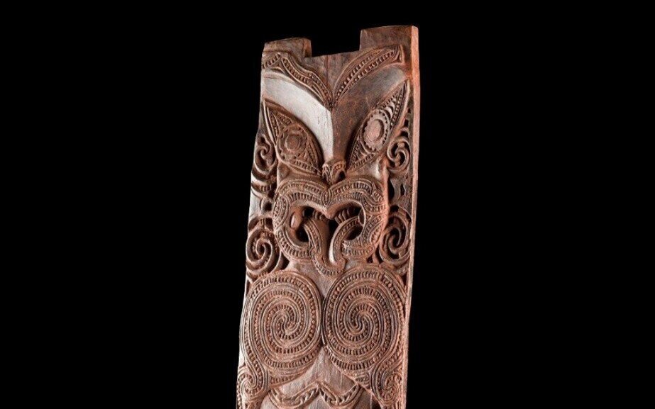 Holzskulptur mit komplexen, spiralförmigen Schnitzereien auf schwarzem Hintergrund.