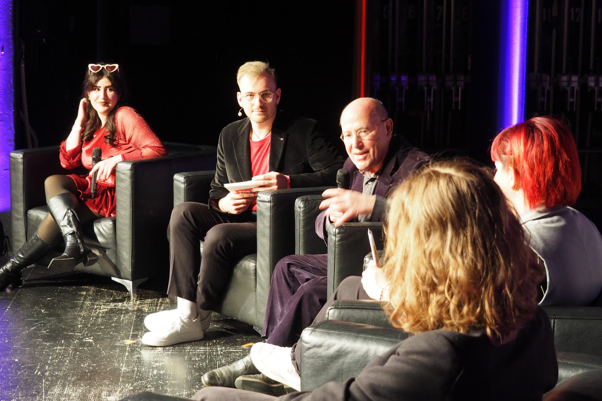 Fünf Personen auf einer Bühne in einem Gespräch. Zwei halten Mikrofone.