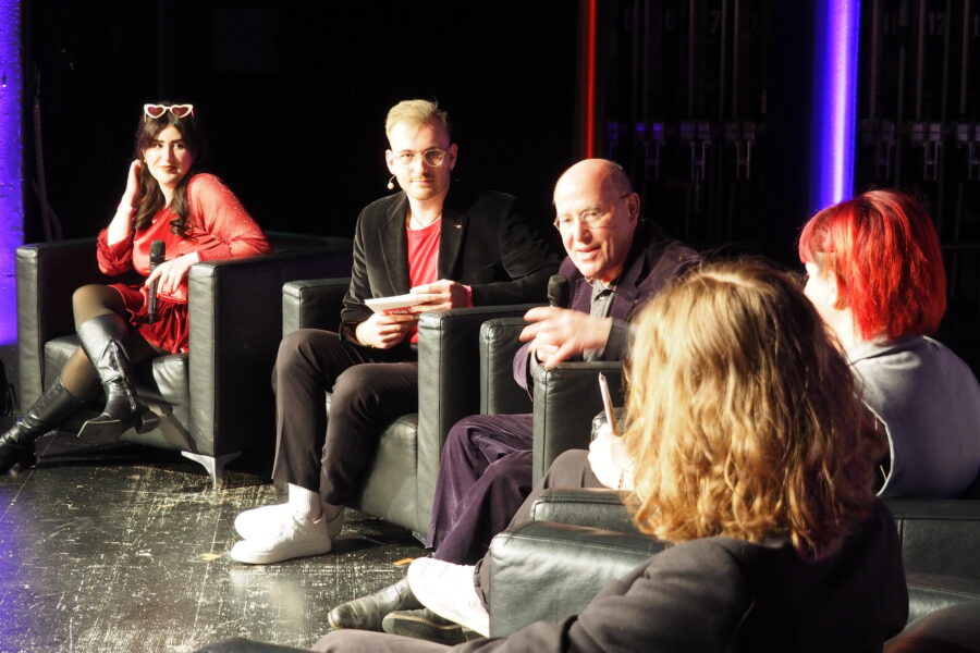 Fünf Personen auf einer Bühne in einem Gespräch. Zwei halten Mikrofone.