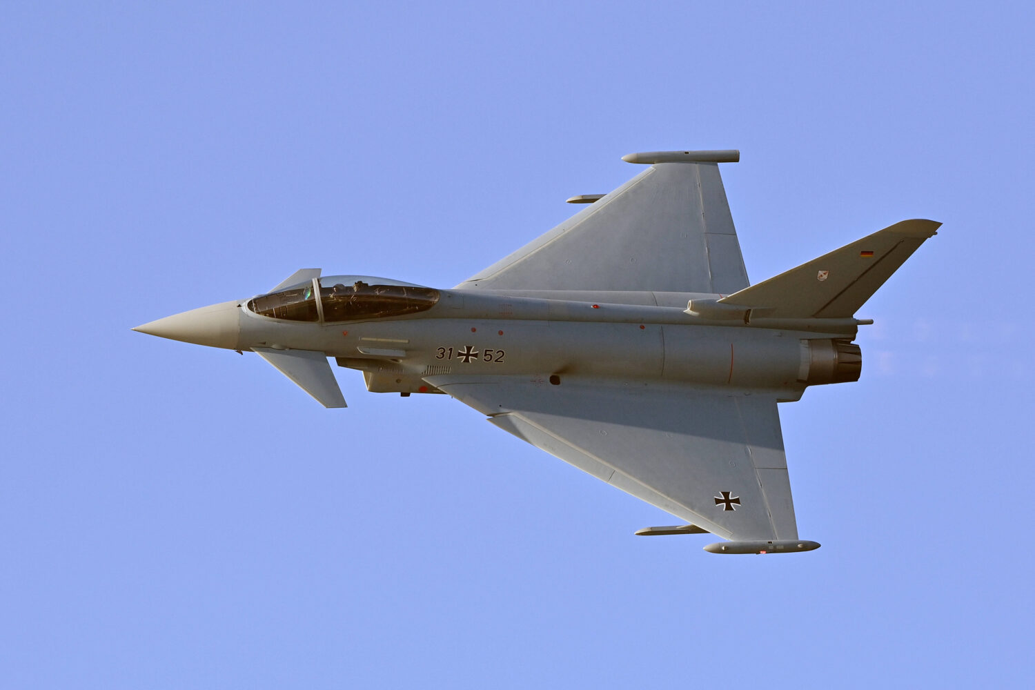 Kampfflugzeug im Flug vor blauem Himmel, seitlich von oben fotografiert.