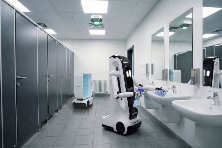 Roboter reinigt in einem öffentlichen Badezimmer mit Waschbecken und Kabinen.