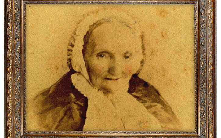 Altes Foto einer lächelnden Frau in Spitze und Umhang, in einem verzierten Rahmen.