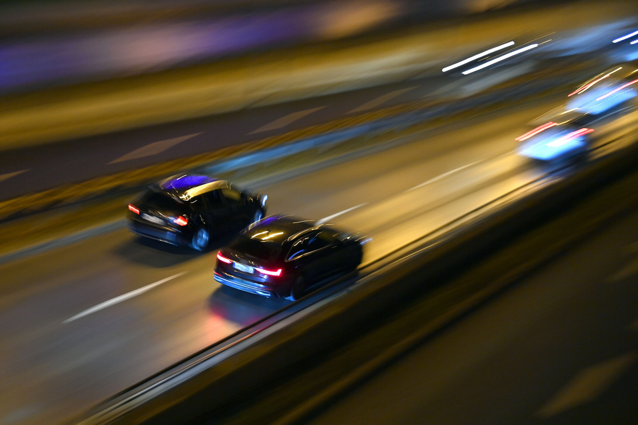 Zwei schwarze Autos fahren bei Nacht auf einer mehrspurigen Straße.