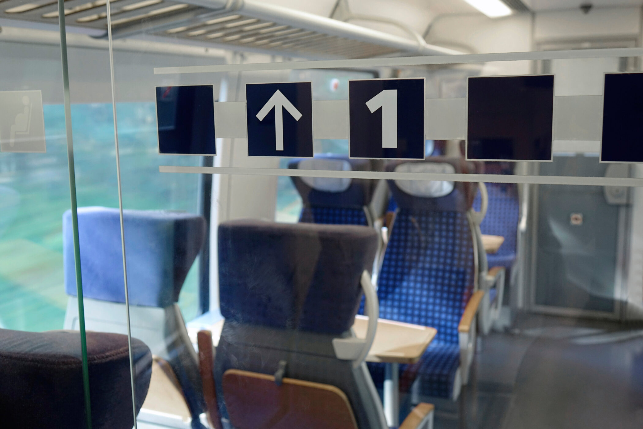 Zugabteil mit blauen Sitzen, Schild mit Pfeil und Zahl 1 an der Glastür.