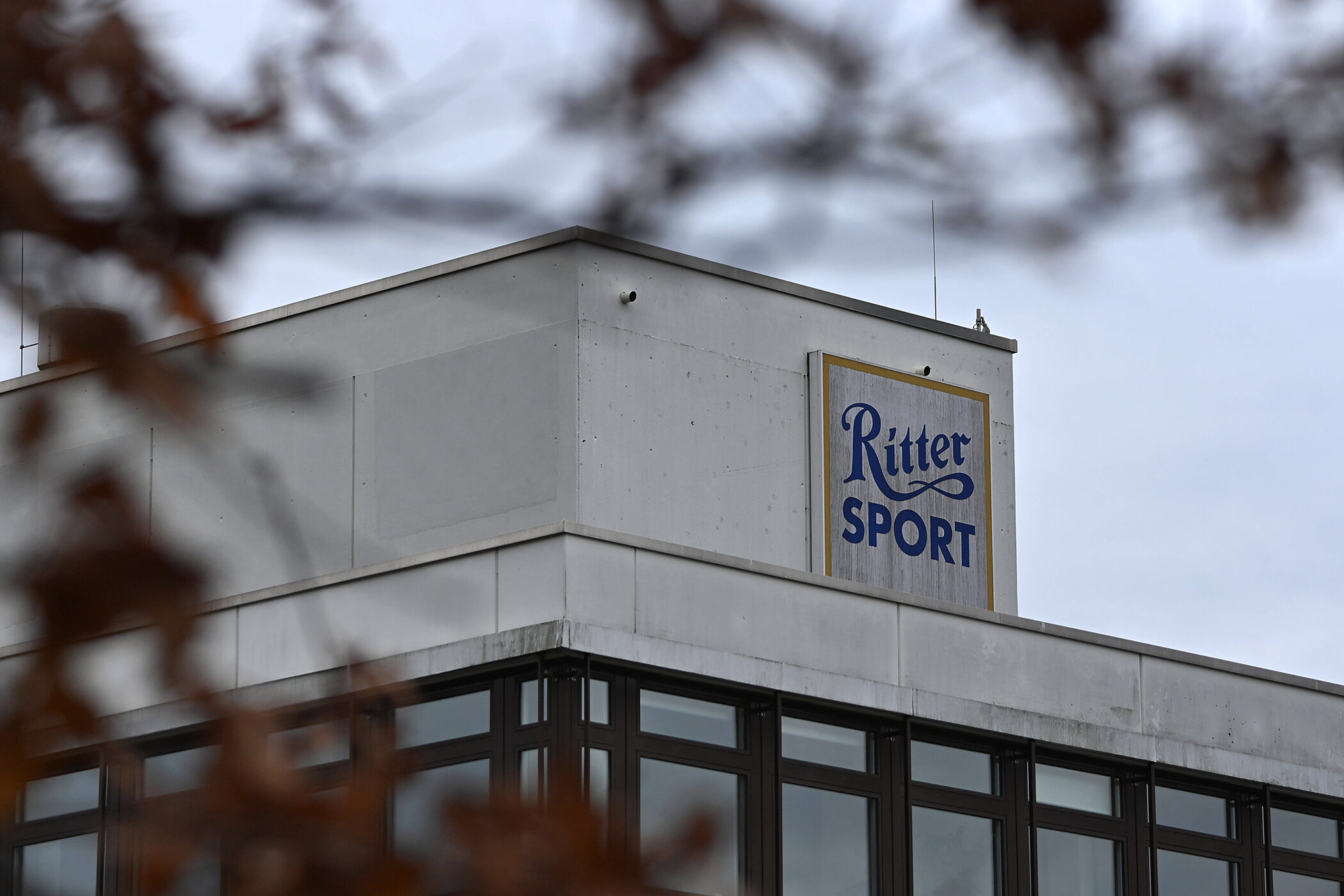 Gebäude mit "Ritter Sport" Schild, im Vordergrund unscharfe Blätter.