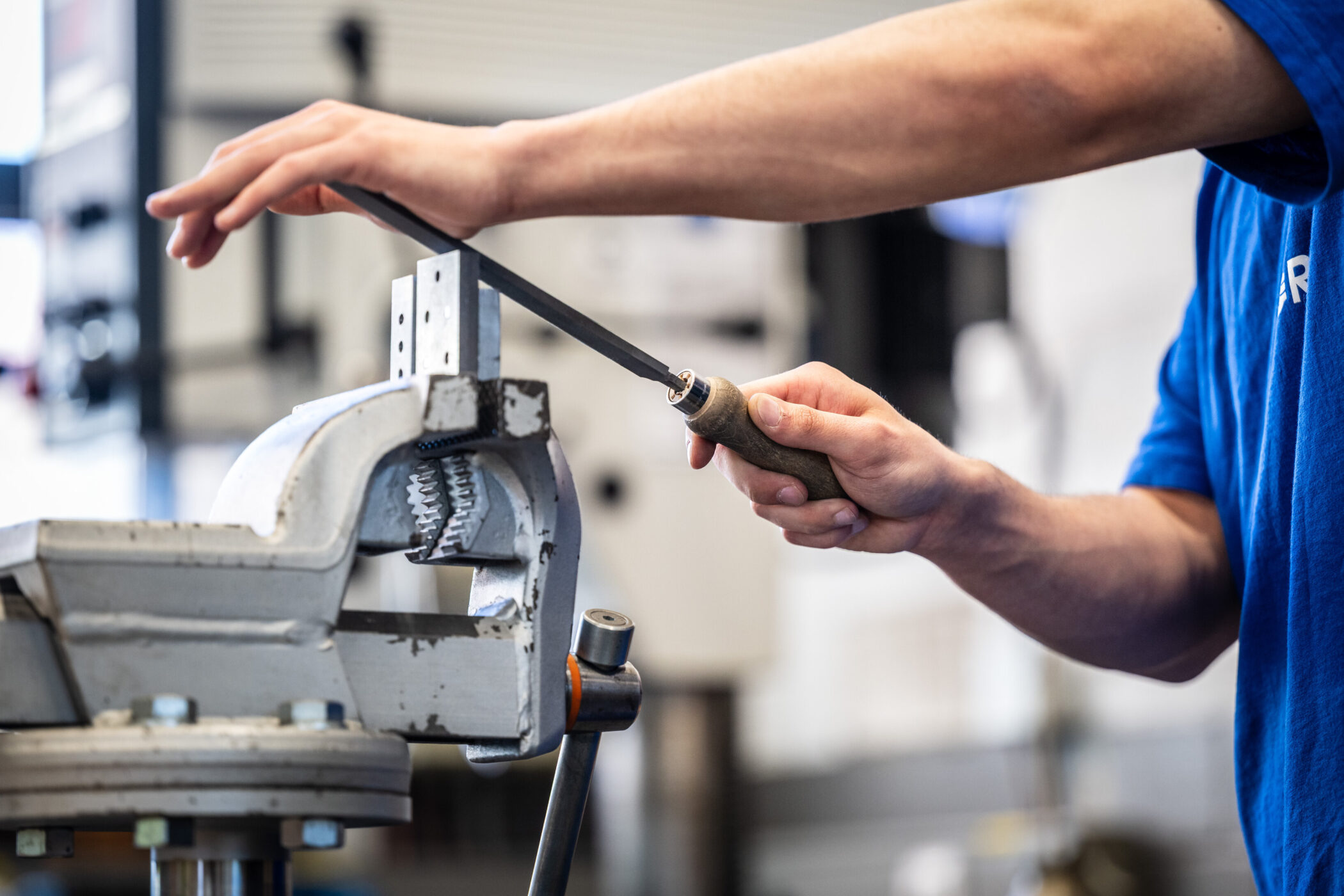 Person feilt Metallstück in Schraubstock.