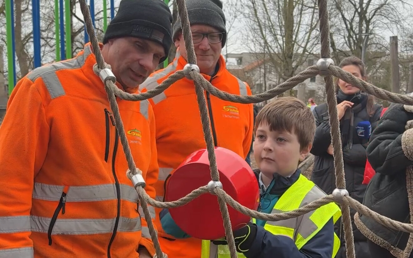 Drei Personen und Kind bei Klettergerüst. Erwachsene in orange Arbeitskleidung.
