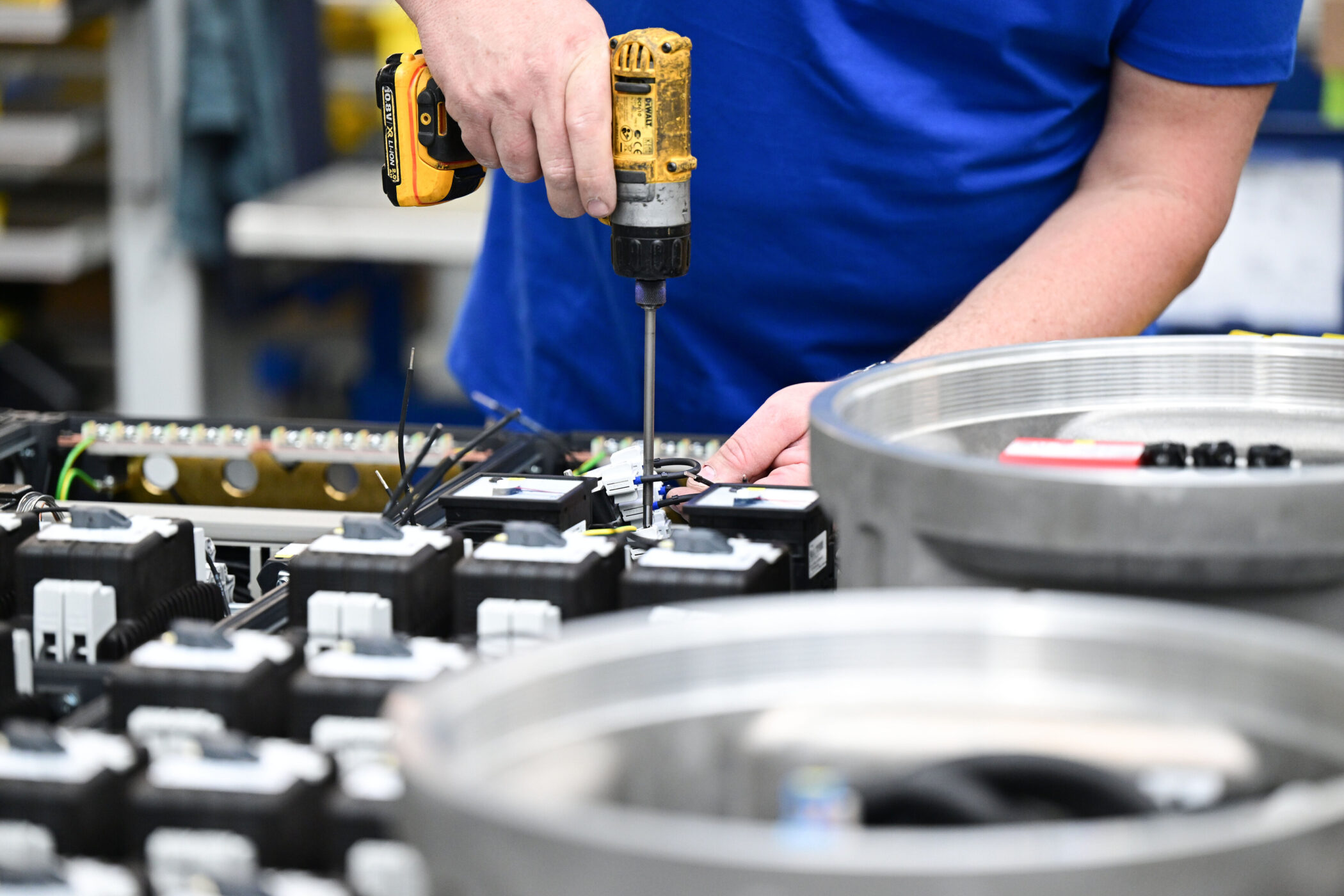 Person in blauem Shirt arbeitet mit Akkuschrauber an elektronischen Bauteilen.