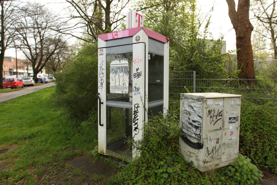 Telefonzelle mit Graffiti, daneben ein Kasten, umgeben von Bäumen und Gras.