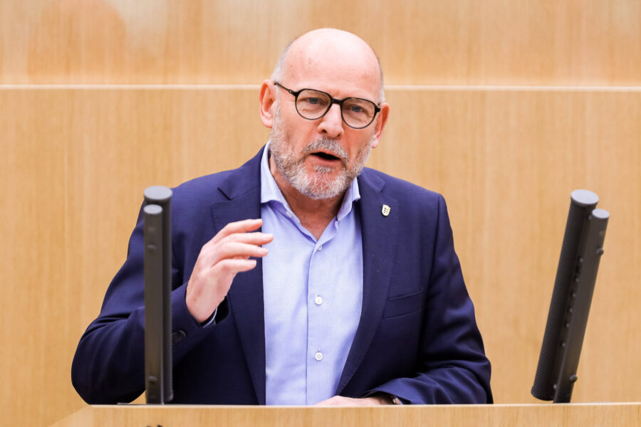 Ein Mann spricht an einem Rednerpult, trägt Anzug und Brille.