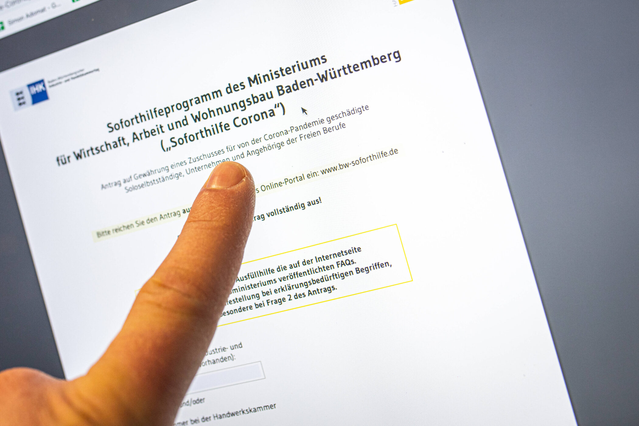 Finger zeigt auf Text über Soforthilfeprogramm Baden-Württemberg auf einem Bildschirm.