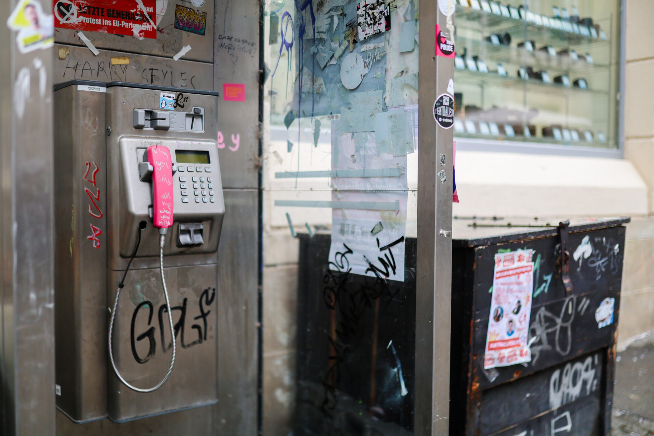 Öffentliche Telefonzelle mit graffiti-beschriebenem Telefonhörer und beklebten Scheiben.