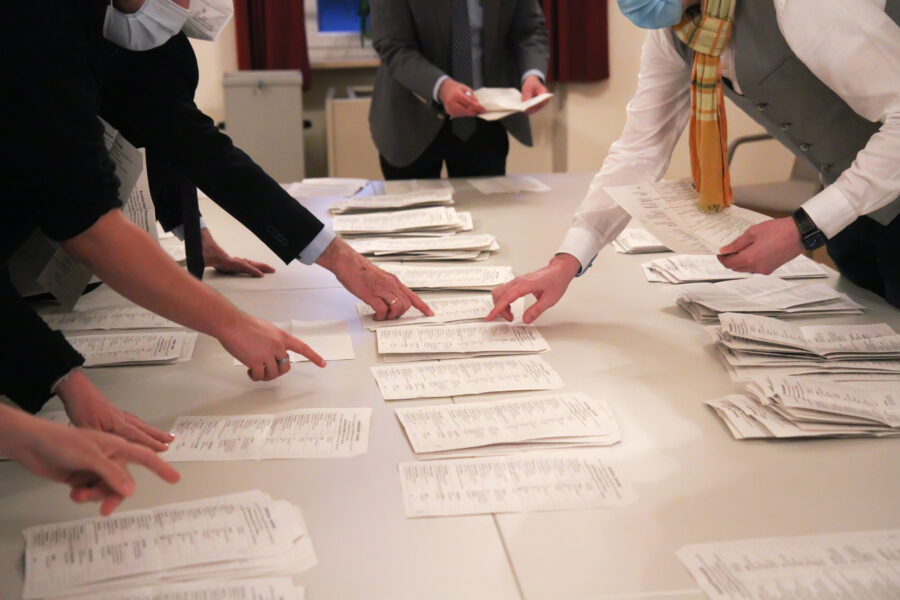 Mehrere Personen zählen Papierstapel auf einem Tisch.