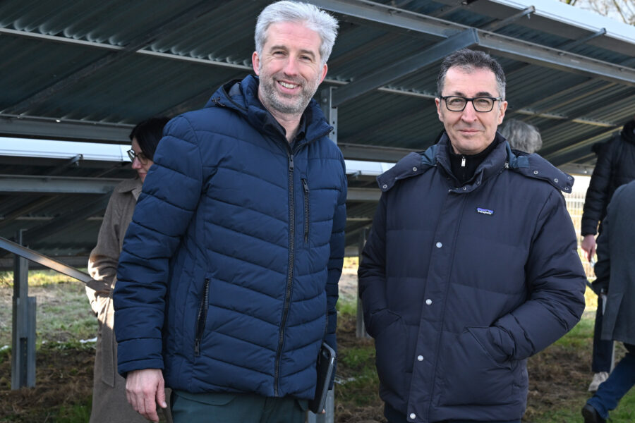 Zwei Männer in Winterjacken stehen vor einer Metallkonstruktion im Freien.