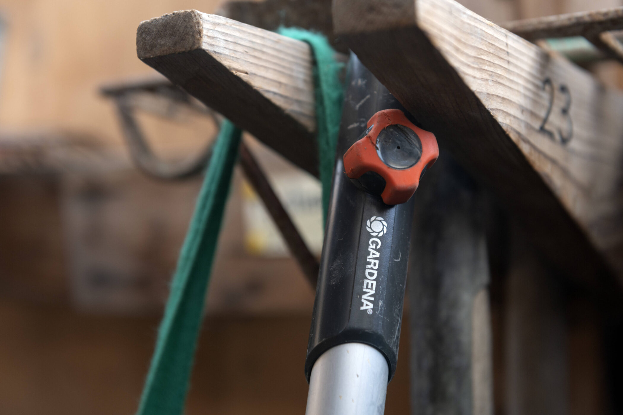 Gartengerät mit rotem Griff und Gardena-Logo, an Holzregal gelehnt.