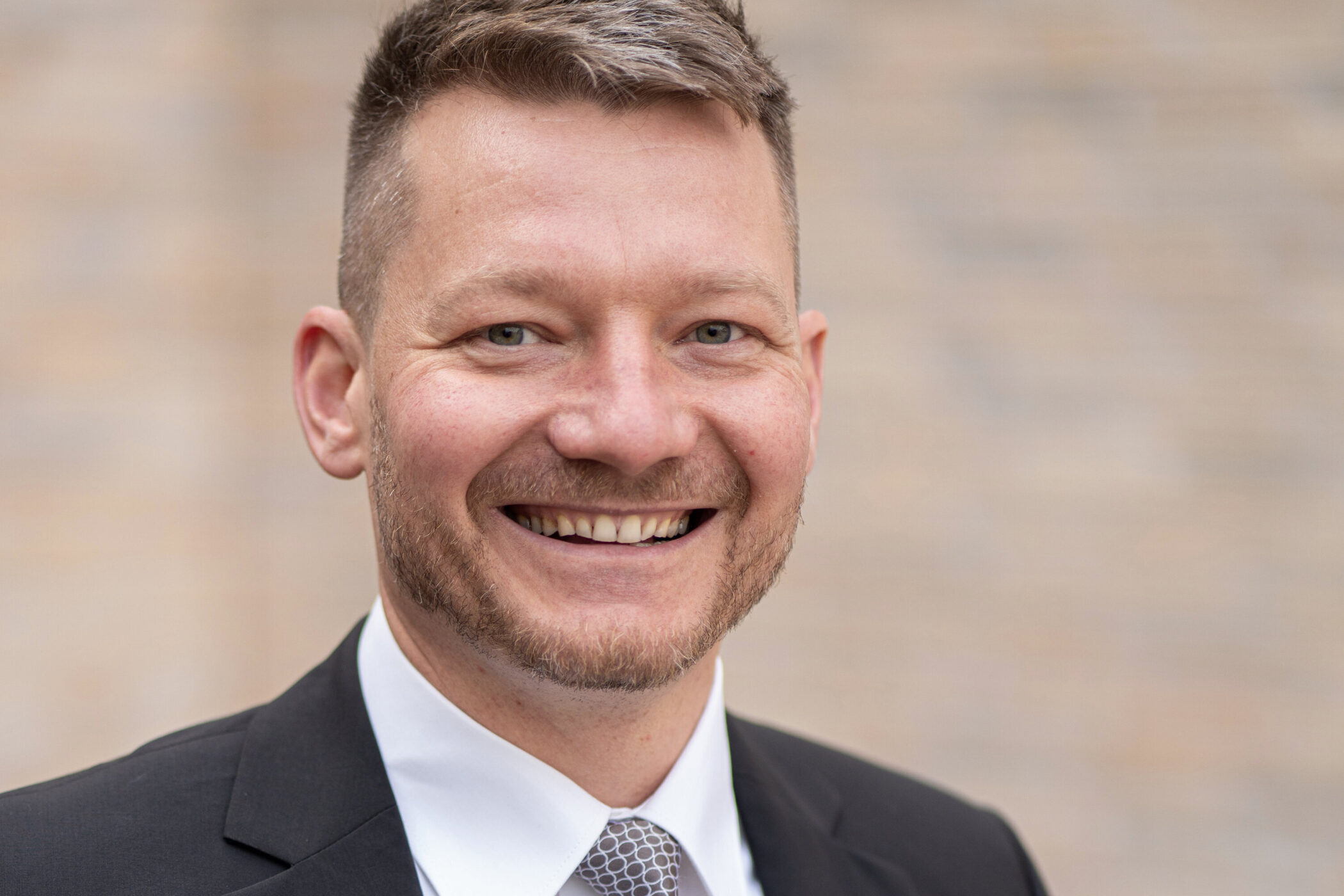 Lächelnder Mann im Anzug vor unscharfem Hintergrund.