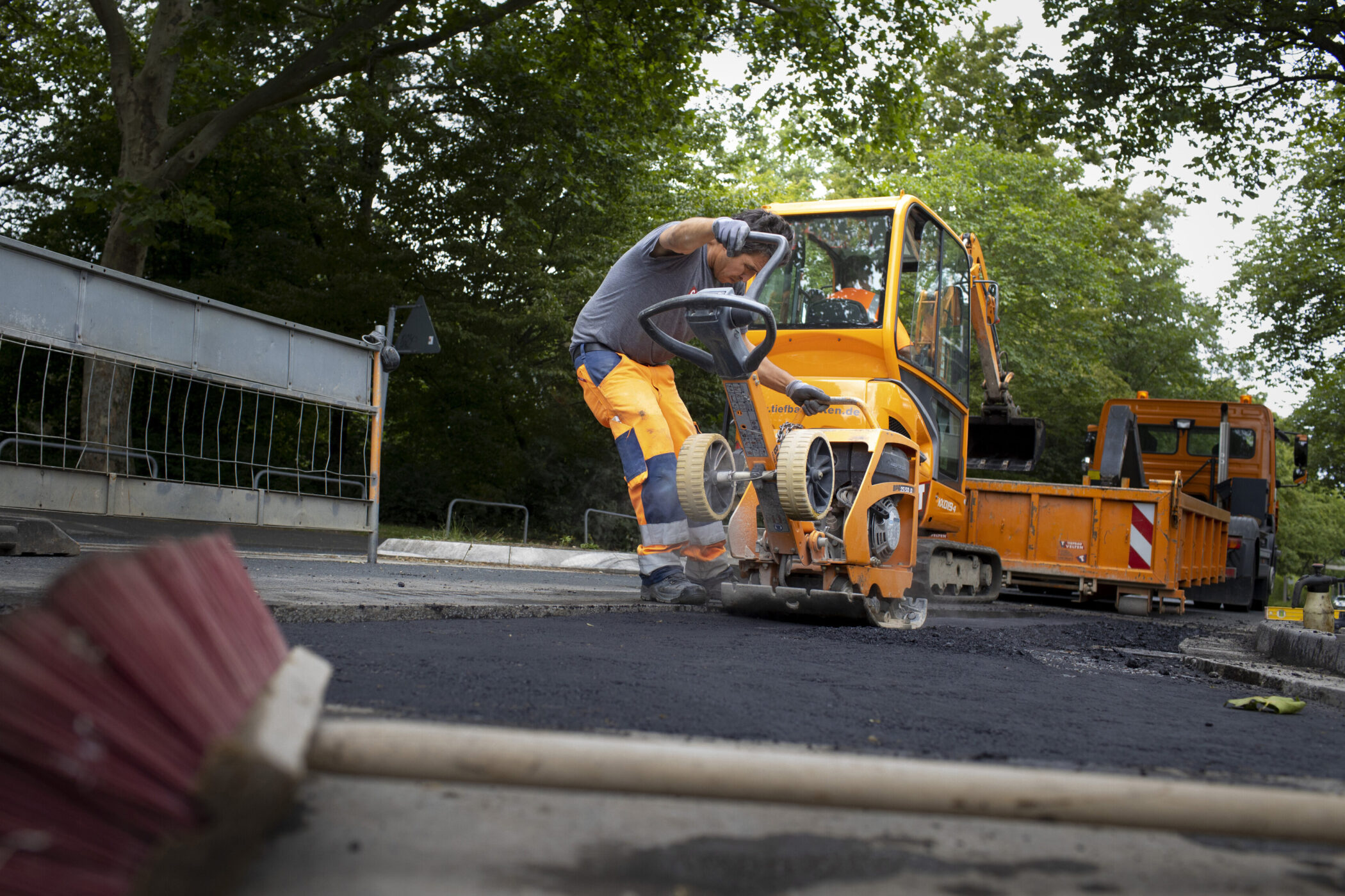 Zwei Arbeiter legen auf einer Straße Asphalt mit großen Maschinen.