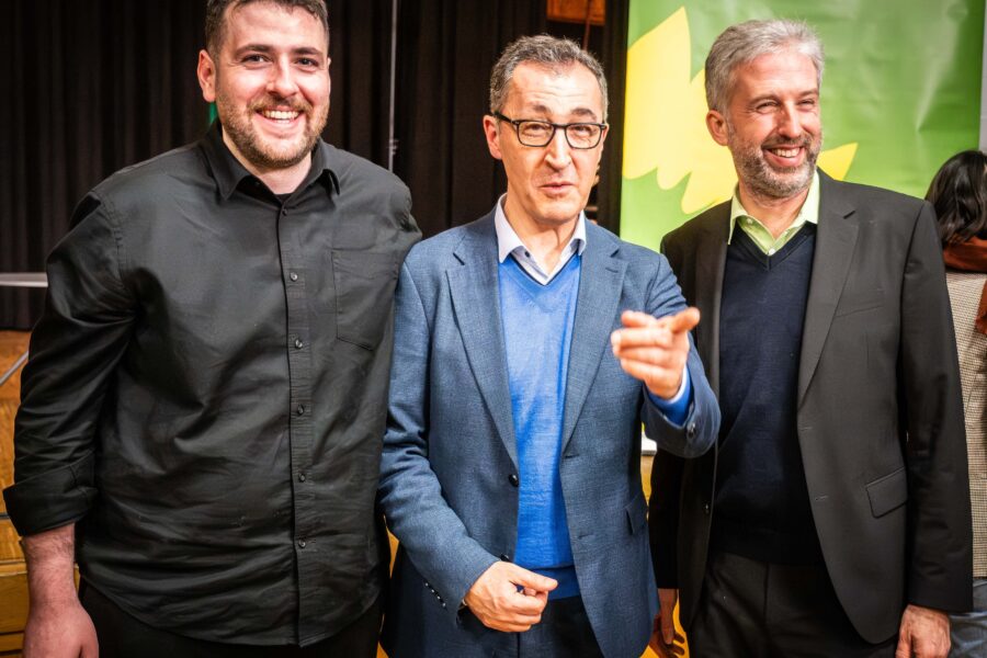 Drei lächelnde Männer stehen nebeneinander, einer zeigt mit der Hand.