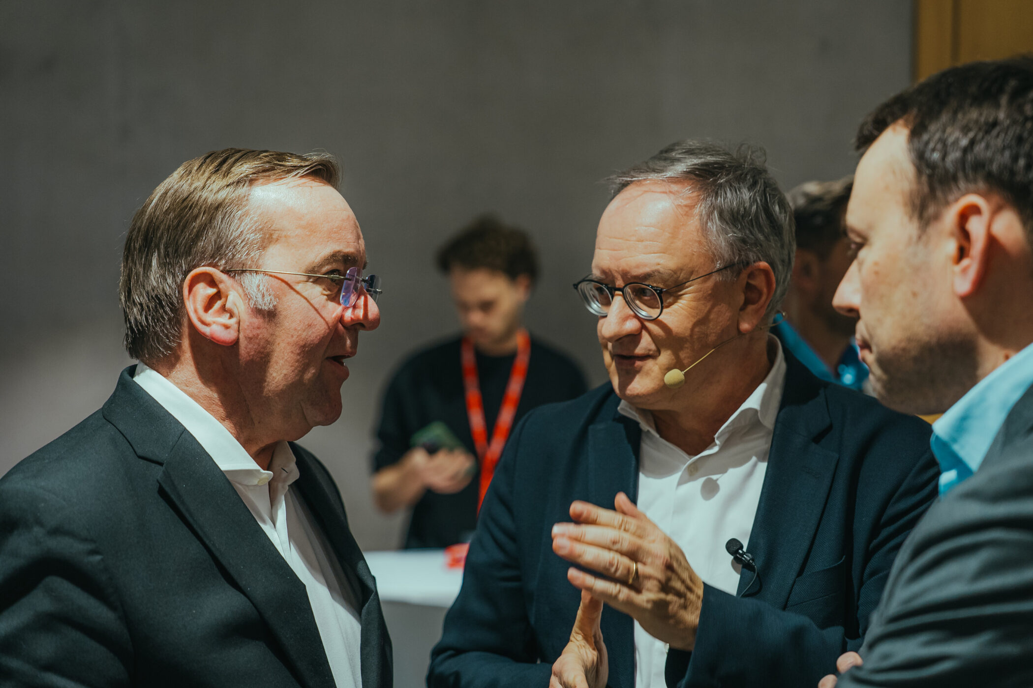 Drei Männer im Anzug im Gespräch, einer trägt ein Mikrofon am Ohr.