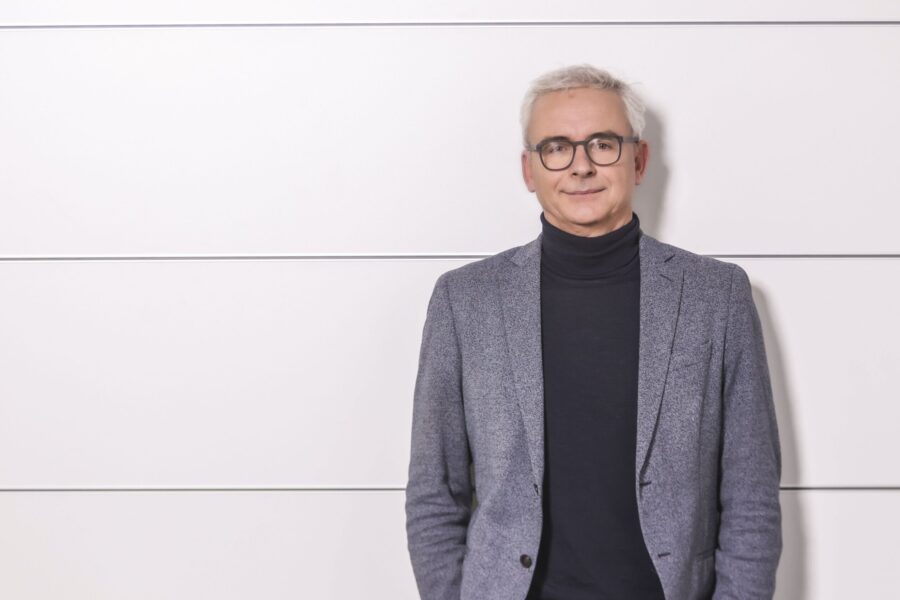 Eine Person mit Brille steht vor einer weißen Wand.