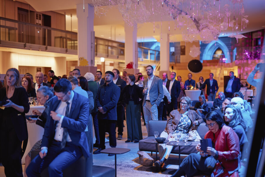 Viele Menschen in eleganter Kleidung in einem beleuchteten Innenraum.