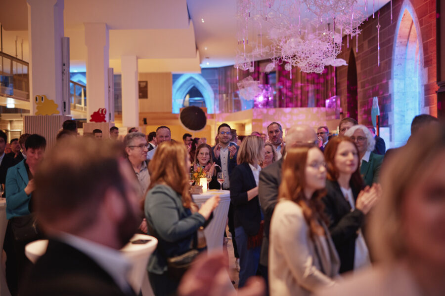 Mehrere Menschen in eleganter Kleidung bei einer Veranstaltung in beleuchtetem Raum.
