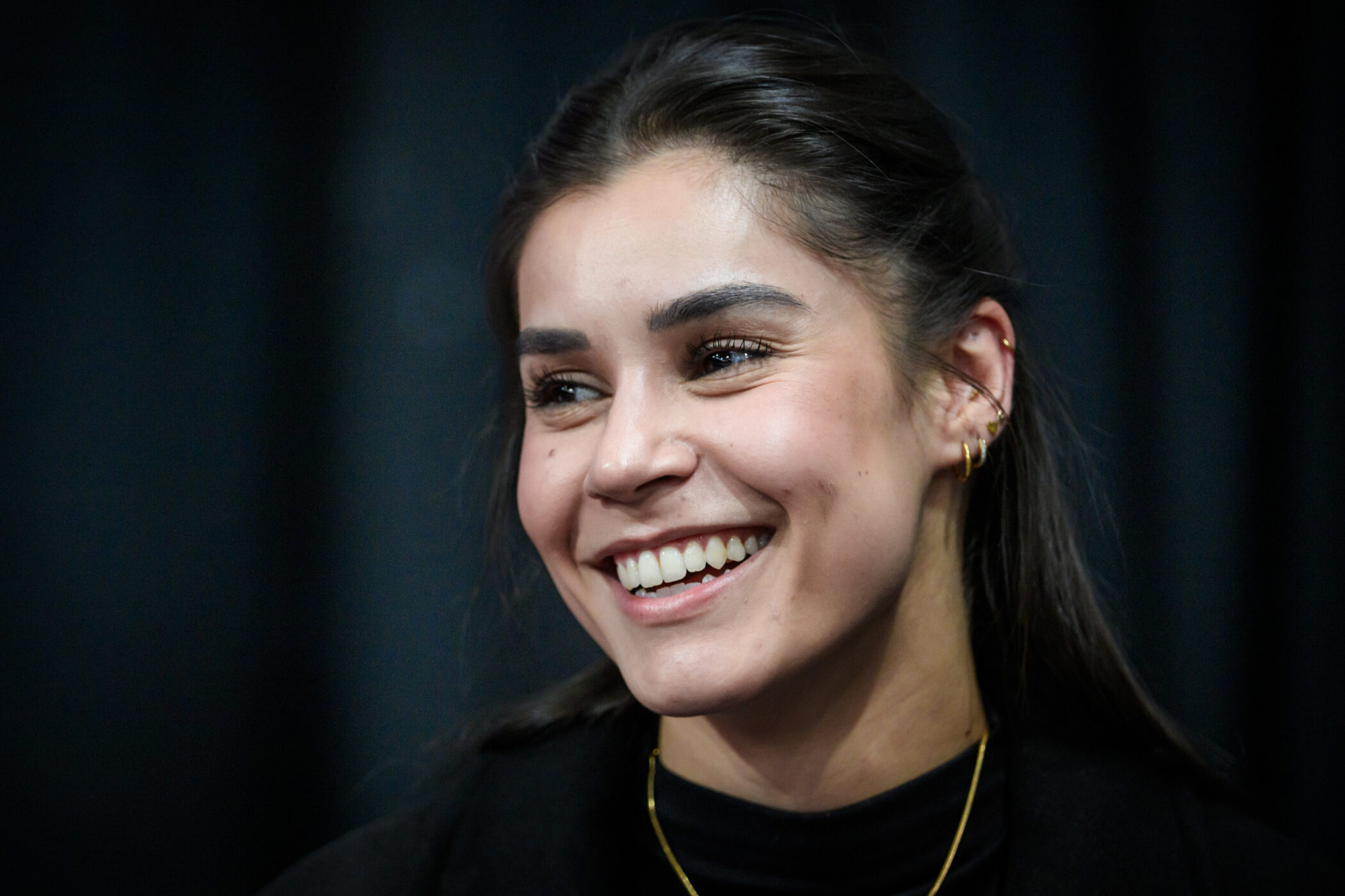 Lächelnde Frau mit Ohrringen vor dunklem Hintergrund.