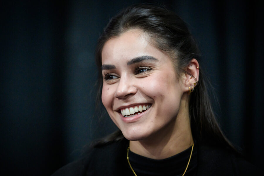 Lächelnde Frau mit Ohrringen vor dunklem Hintergrund.