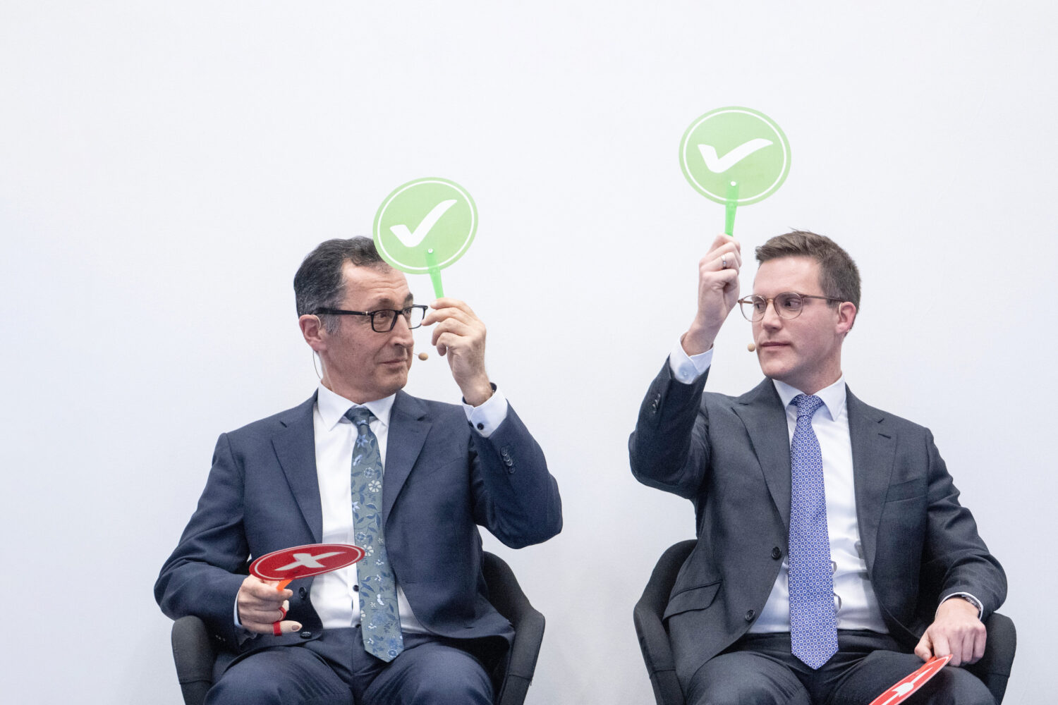 Zwei Männer im Anzug halten grüne Häkchen-Schilder hoch und rote Kreuz-Schilder unten.