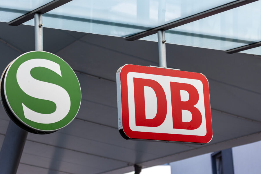 Grünes S-Bahn-Schild und rotes DB-Schild unter Glasdach.