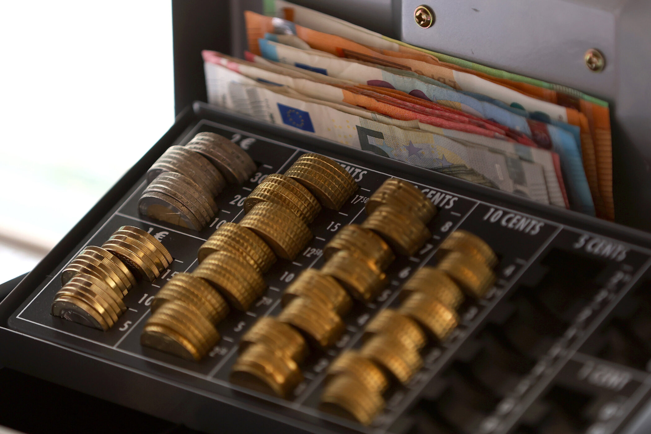 Münzen und Geldscheine in einer geöffneten Kassenlade.