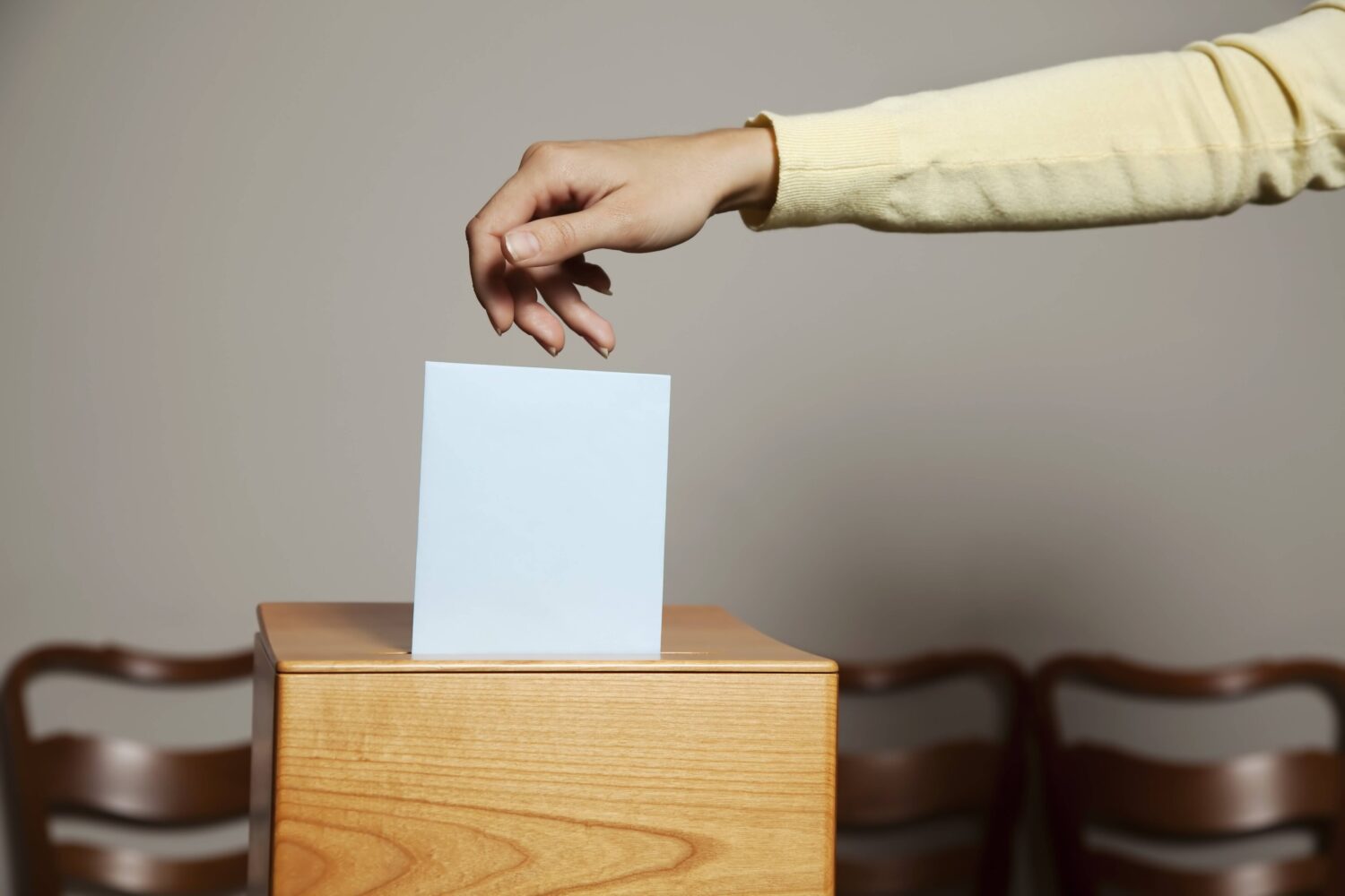 Hand wirft einen weißen Zettel in eine Holzurne.