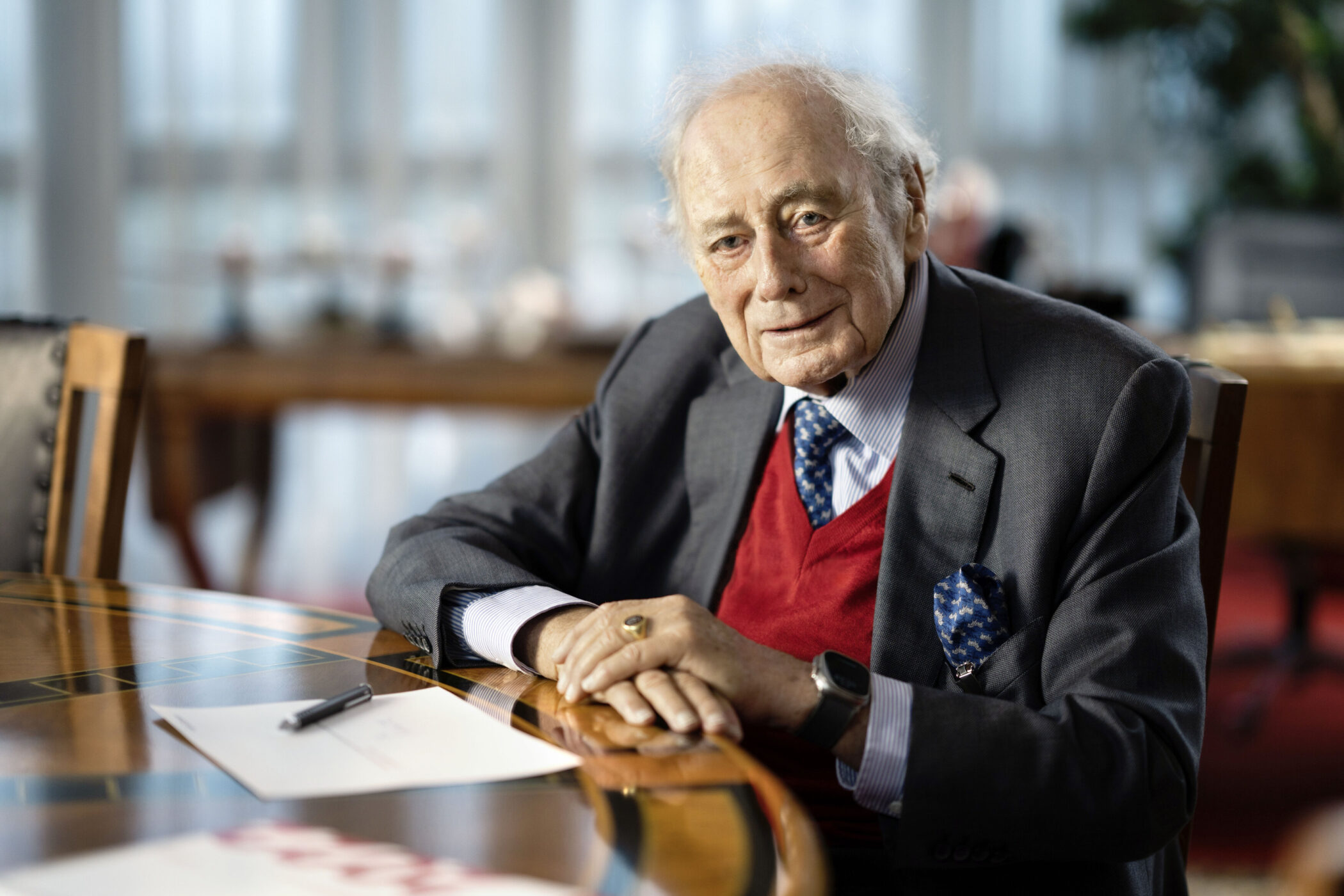 Älterer Mann in Anzug, sitzt am Tisch mit Papier und Stift.