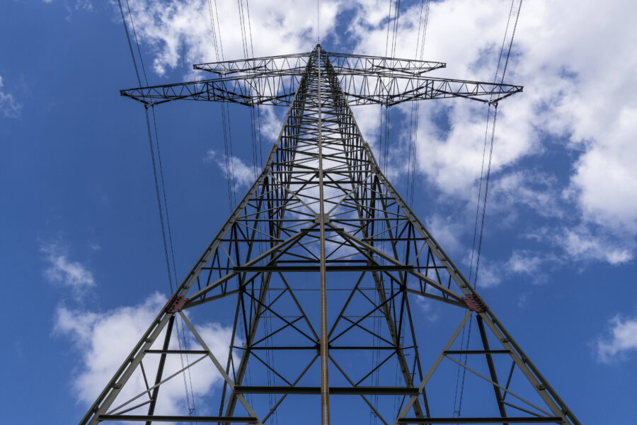 Strommast von unten, verstrebtes Metallgerüst vor blauem Himmel mit Wolken.