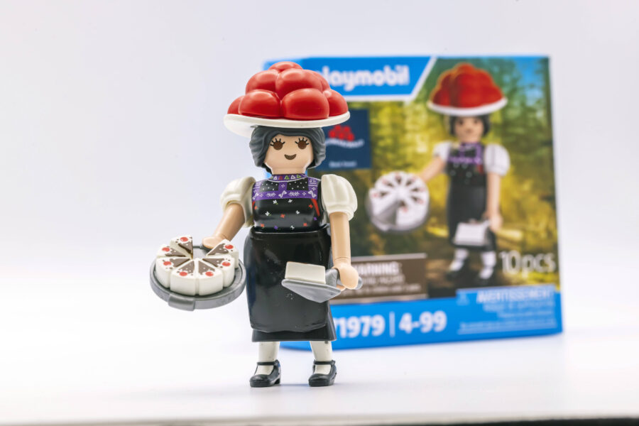 Spielzeugfigur mit rotem Hut hält eine Torte und ein Tablett. Verpackung im Hintergrund.