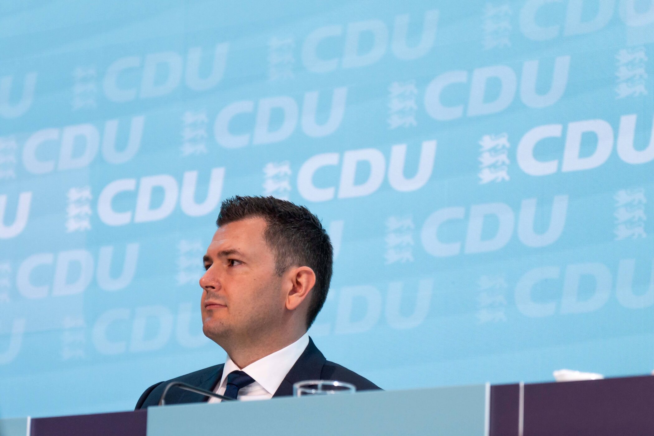 Ein Mann im Anzug sitzt vor einer blauen Wand mit CDU-Logo.