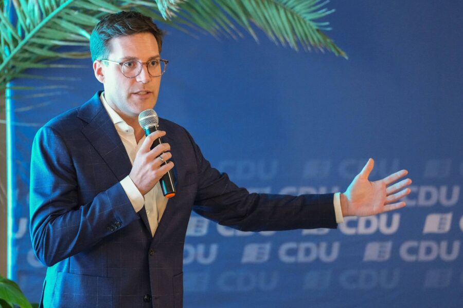 Mann in Anzug hält Mikrofon, Hintergrund zeigt CDU-Logo.